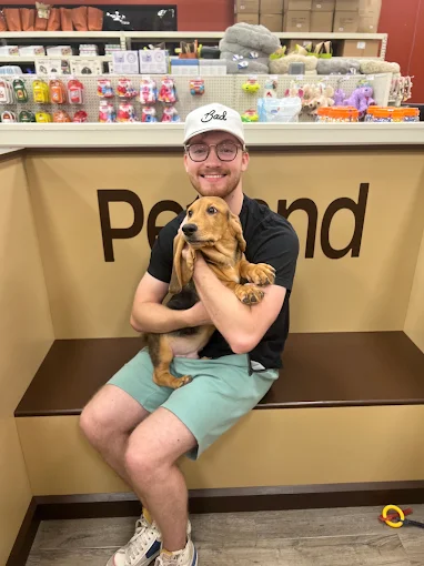Man seated on a Petland bench holding a brown puppy